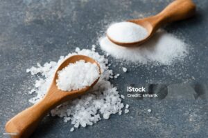 Two salt types in wooden spoons on dark background.